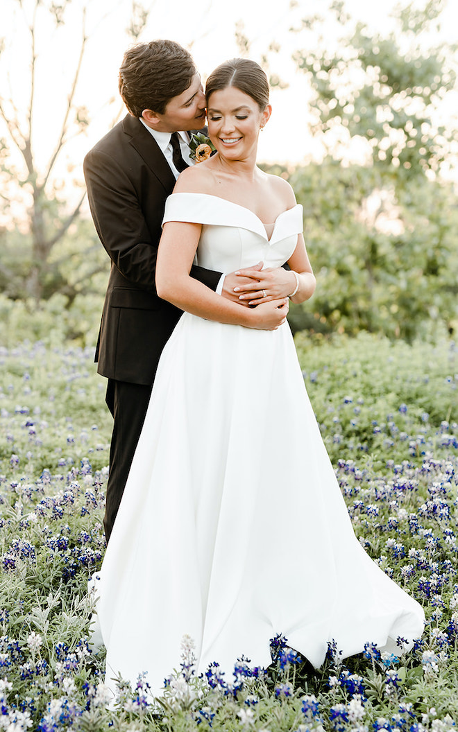 The bride and groom pose for their wedding portraits in a field of bluebonnets at sunset. 