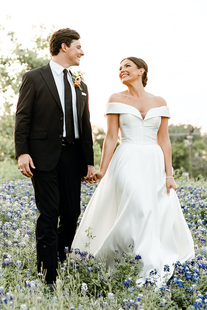 The bride and groom hold hands and smile at each other in a field of bluebonnets.
