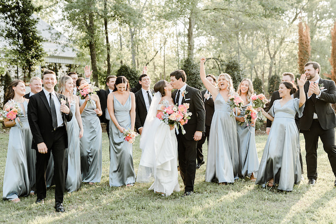 bride and groom kissing while bridesmaids and groomsmen cheer on a spring day at a Houston wedding day.