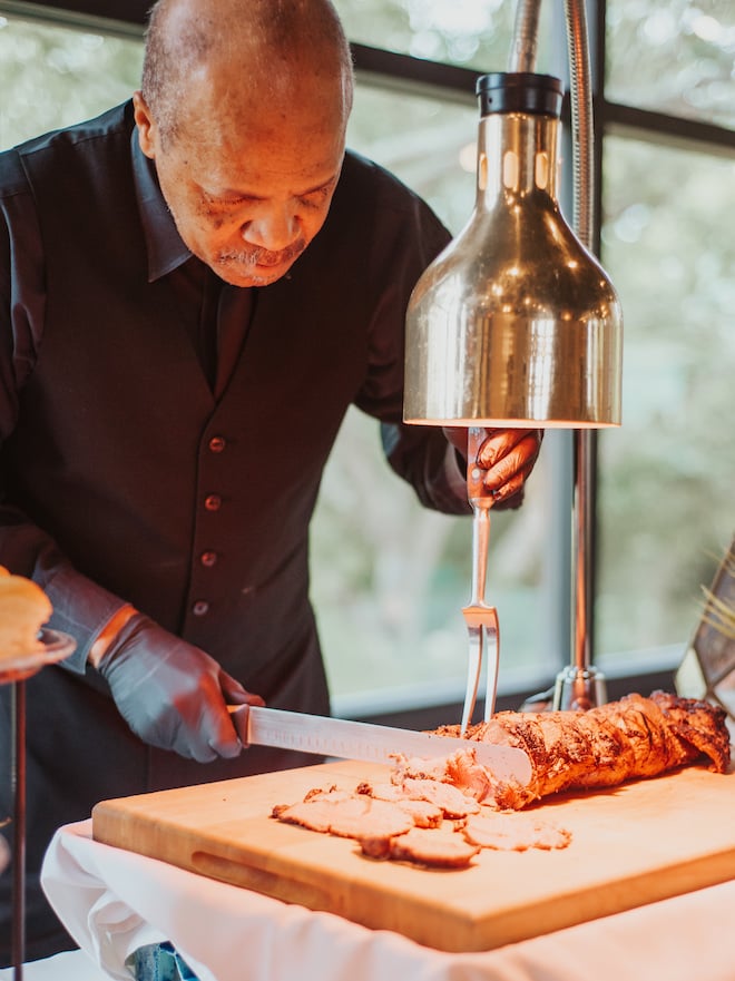 A team member from Bailey Connor Catering cuts steak at a food station for wedding guests.