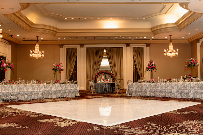 A white dance floor in between two long tables in pink and gray linens in the glam hotel ballroom.
