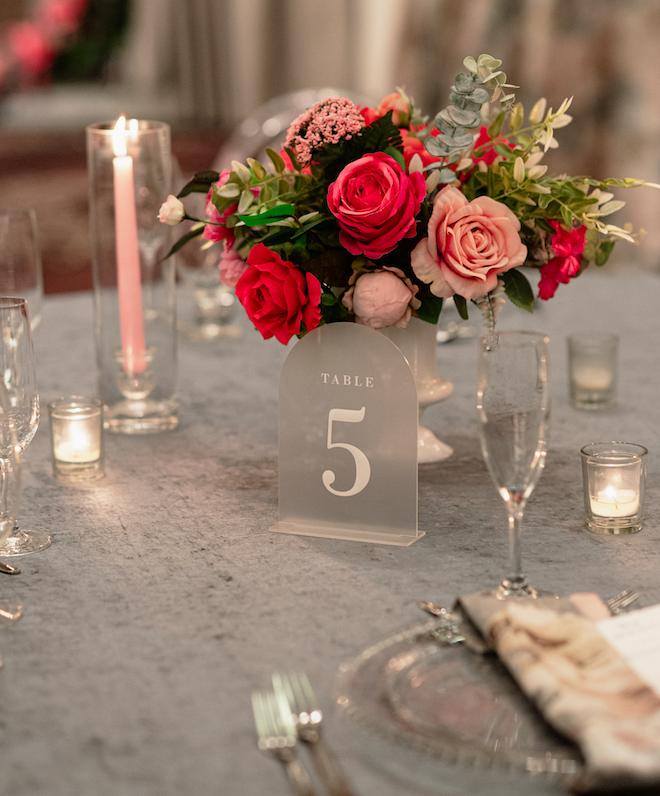 A sign that says "Table 5" with a pink bouquet centerpiece and pink candles. 
