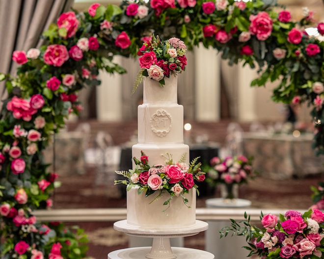 A four-tier white cake with a monogram and pink florals decorating the top and bottom tiers. 