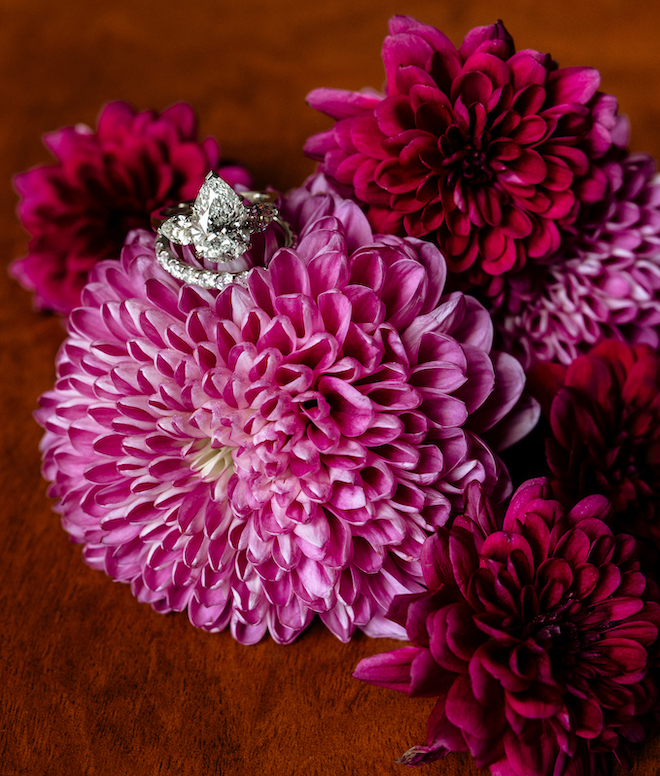 A pear-shaped diamond engagement ring and diamond band resting on pink florals. 