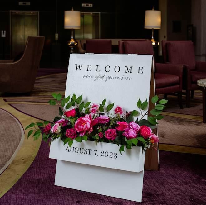 A white welcome sign in the Hilton Houston Post Oak lobby with the date, August 7th, 2023, and pink florals with greenery. 
