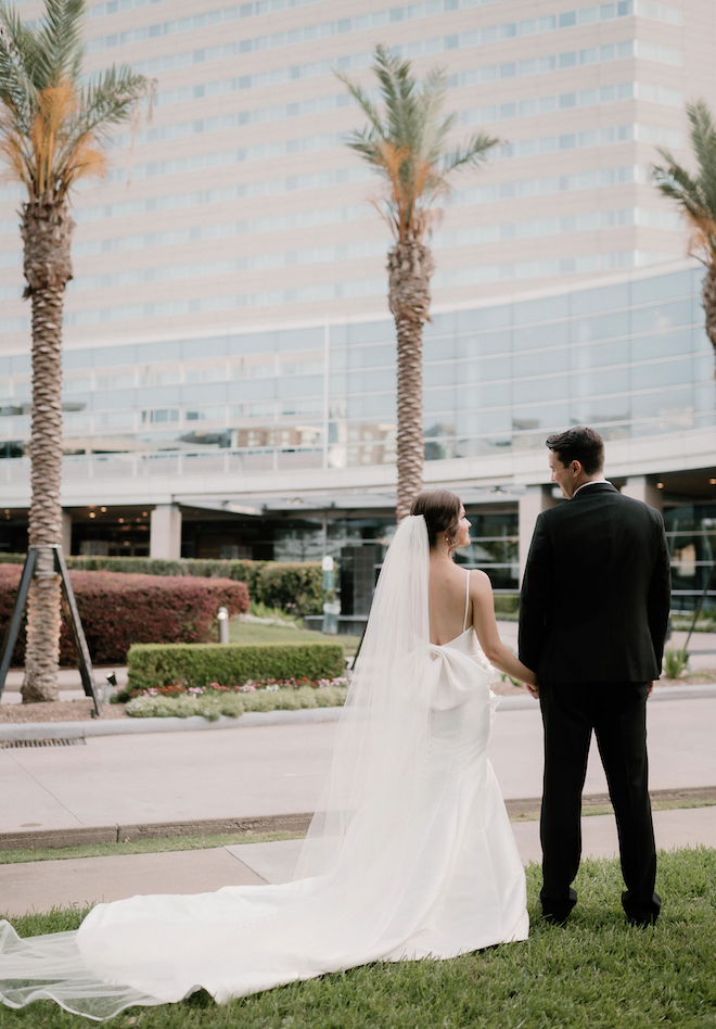 A bride and groom holding hands and looking at each other in front of the Royal Sonesta Houston Galleria.