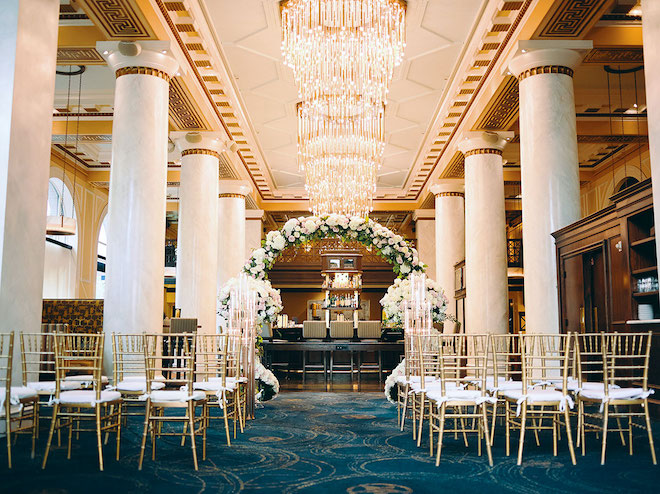 A wedding ceremony in the Hotel Icon lobby with gold chairs and a floral installation. 