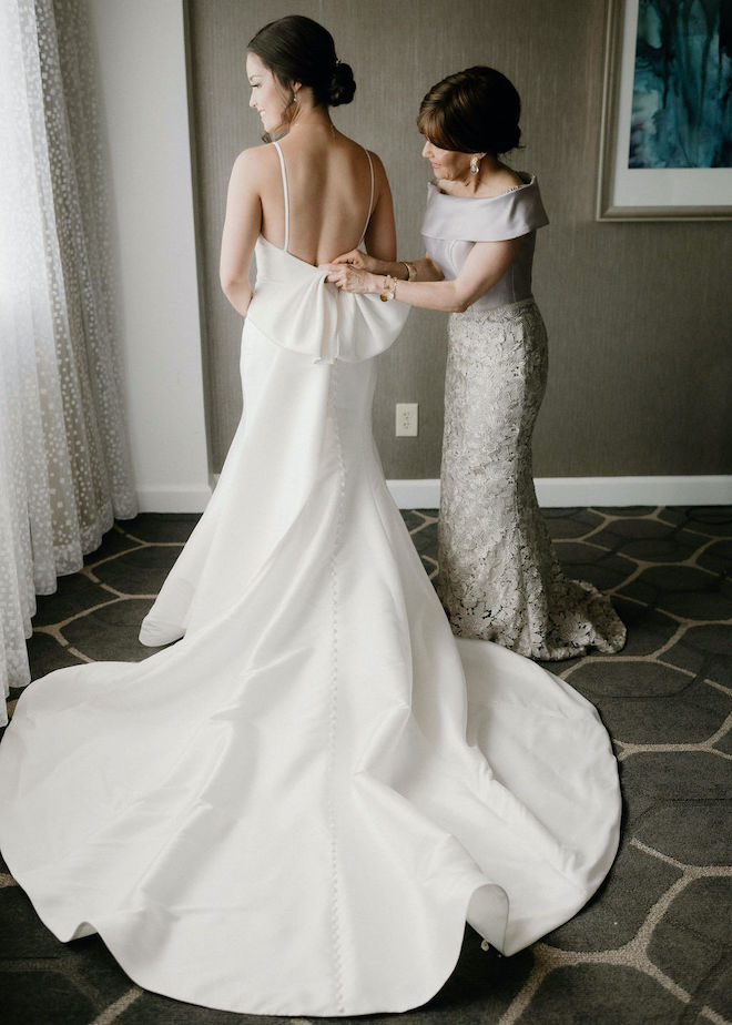 The mother of the bride adjusting the bow on the back of the bride's wedding gown. 