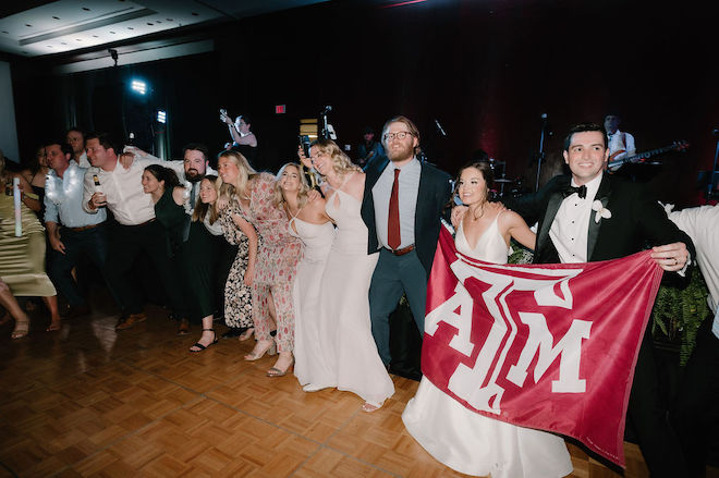 The bride and groom holding up a Texas A&M flag and dancing with guests. 