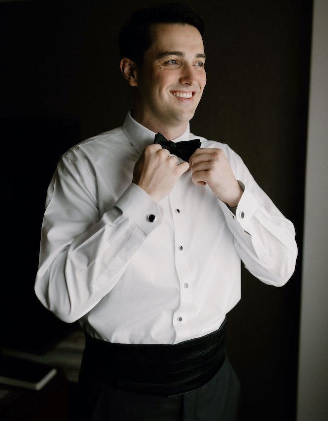 The groom smiling adjusting his bow tie. 