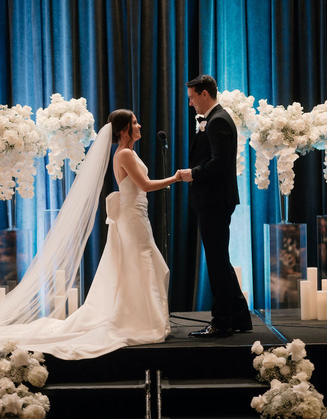 The bride and groom smiling holding hands at the altar. 