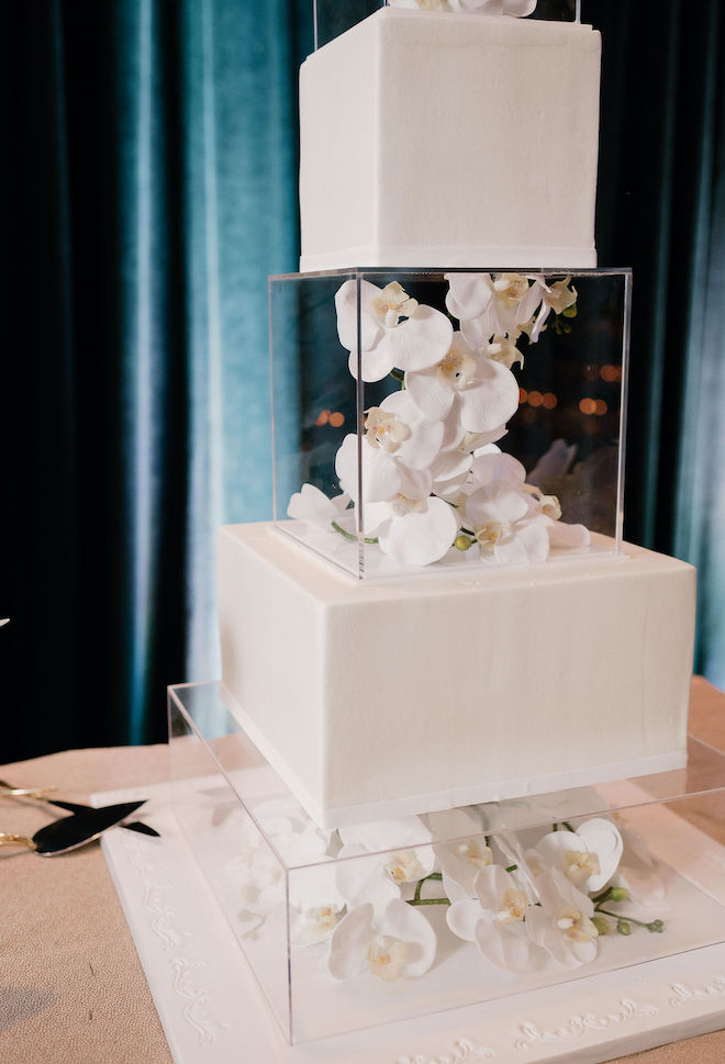 A white wedding cake with two acrylic separators with orchids in them.