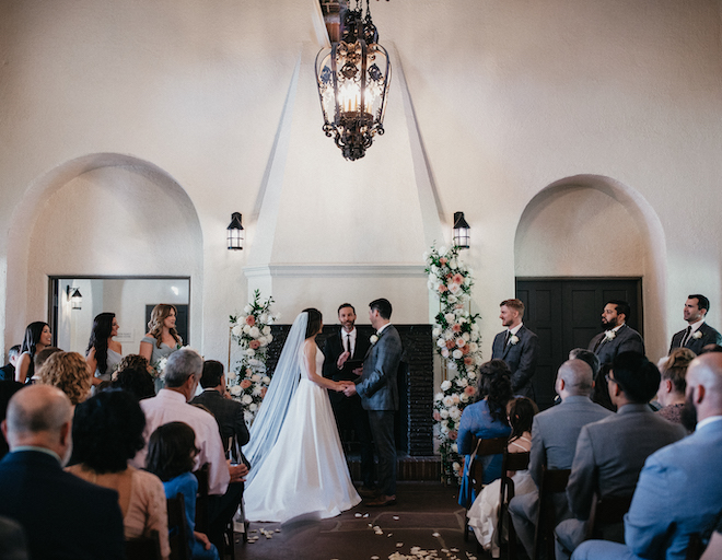 The bride and groom hold hands at the altar at their pink, green, sage and salmon colored wedding. 