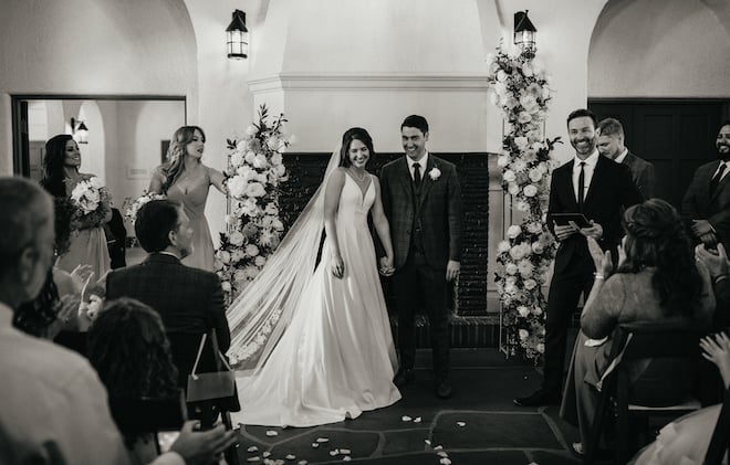 A black and white photo of the bride and groom holding hands as they walk down the aisle as husband and wife. 