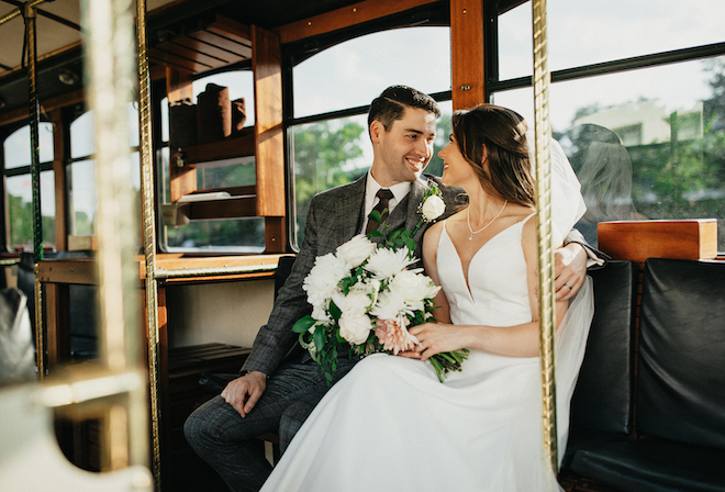The bride and groom look at each other smiling as they ride a trolley to their wedding reception at the Houston Museum of Natural Science. 