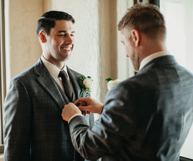 A groomsmen helps button up the grooms suit as they are getting ready for the wedding. 
