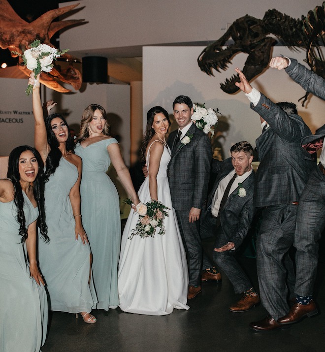 The bride and groom celebrate with their bridal party under the dinosaur fossils at their Houston Museum wedding reception. 