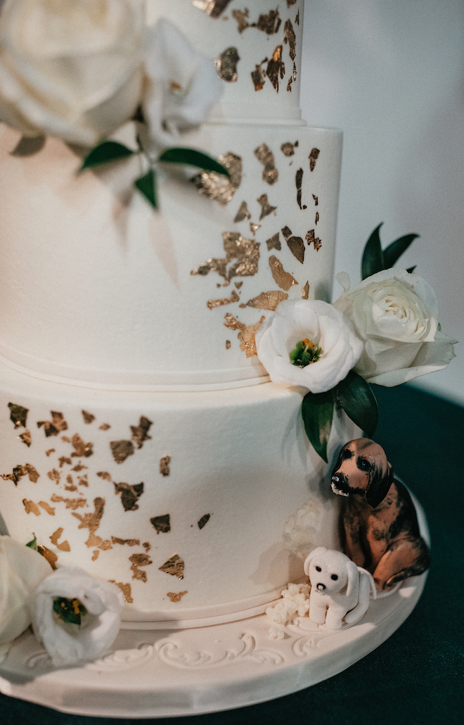 The wedding cake is decorated in white roses, gold flakes and two fondant made dogs. 