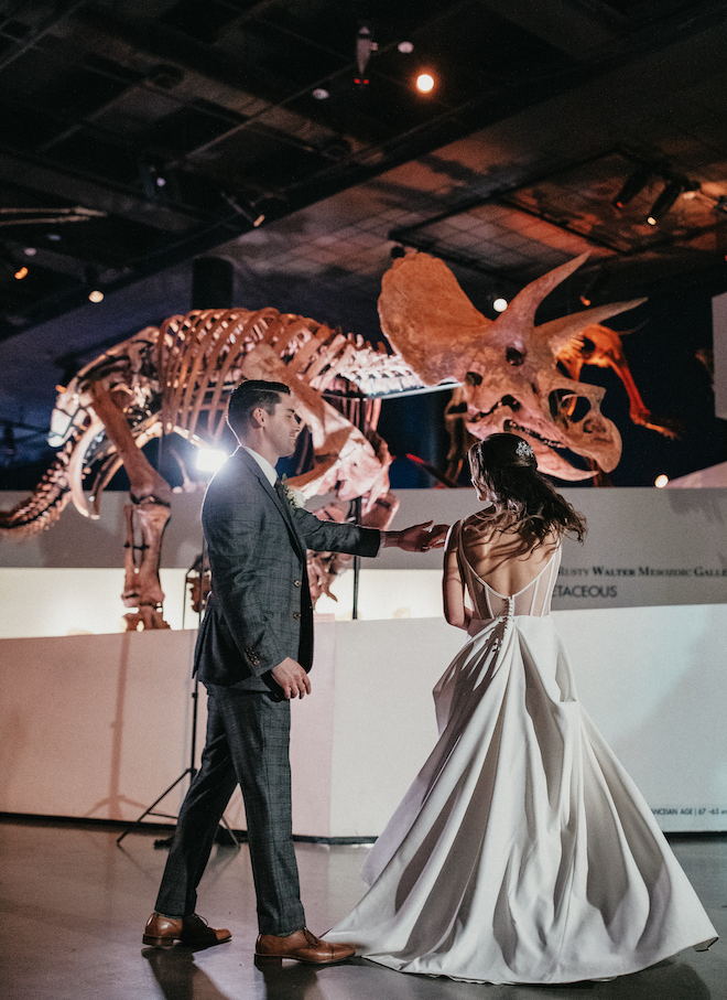 The groom spins the bride on the dance floor under the dinosaur fossils at their wedding reception. 