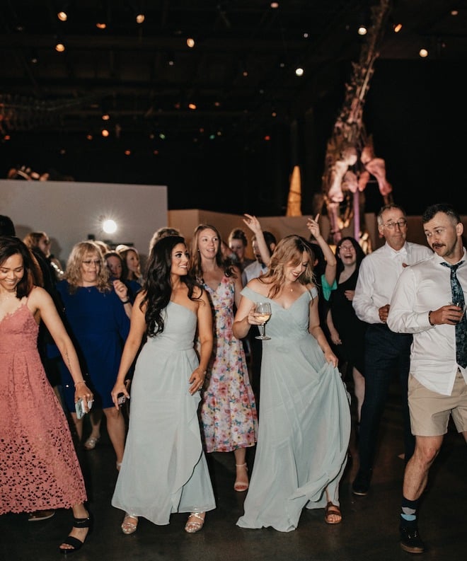 Wedding guests dance on the dance floor under the dinosaur fossils at the Houston museum. 