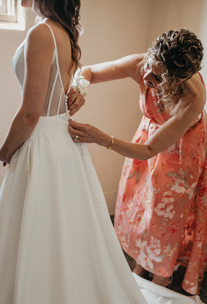 The bride's mother helps her daughter zip into her white wedding gown. 