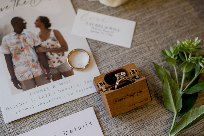 A wooden brown box holding the brides wedding ring with the phrase "it was always you," lays next to the couples wedding stationary.