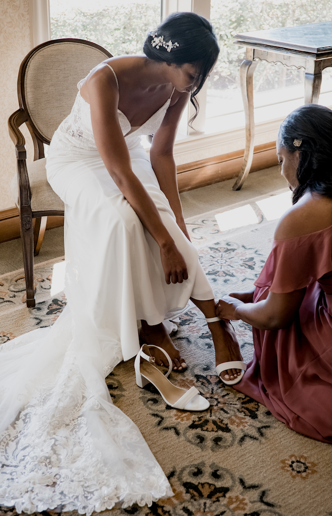 A bridesmaids helps the bride put on her white kitten heels before walking down the aisle at the Royal Oaks Country Club.