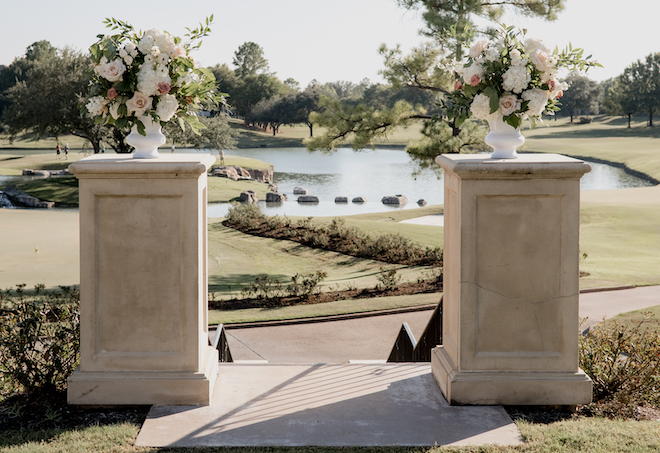 White, pink and greenery floral arrangements decorate the wedding alter for the black, gold and white alfresco ceremony. 