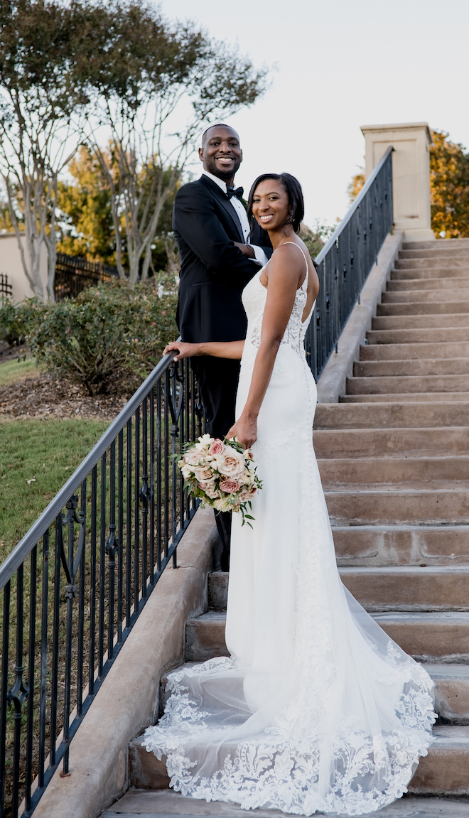 The bride and groom smile on the stairs outside of their wedding venue, the Royal Oaks Country Club.