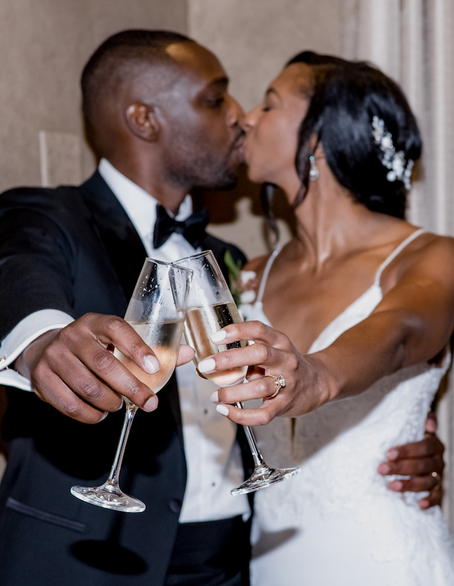 The bride and groom share a kiss while they cheers with a glass of champagne. 