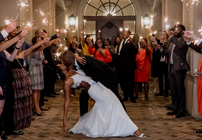 The groom dips the bride for a kiss as guests celebrate with sparklers at the couple's grand exit. 