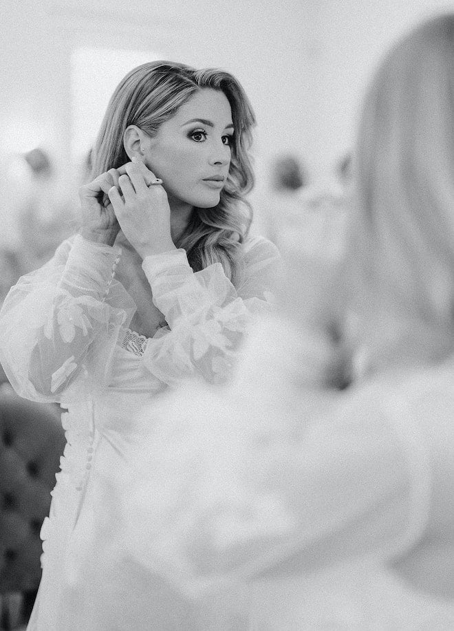 The bride looking in the mirror putting on an earring. 