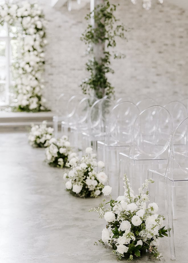 Acrylic chairs with white and greenery bouquets at the end of each row. 