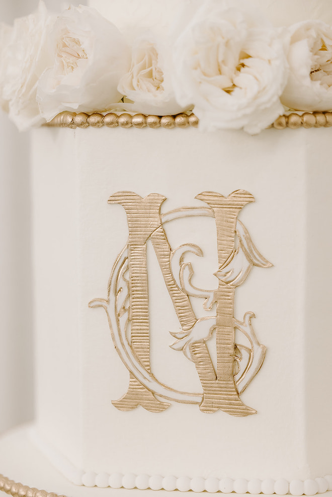 A gold monogram on the white wedding cake. 