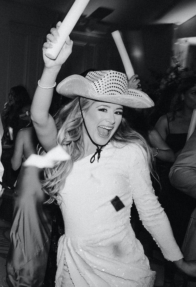 The bride dancing in a sparkly dress with a cowboy hat on and a glow stick.