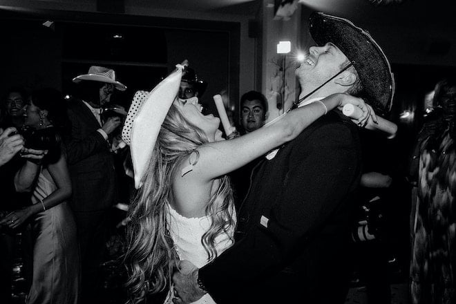 The bride and groom dancing with cowboy hats on. 