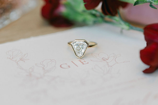 A yellow-diamond engagement ring from Shaftel Diamonds lays on the pastel pink wedding invitation. 