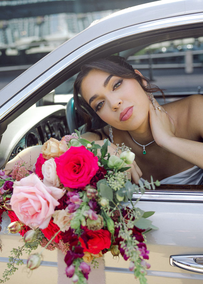 The bride poses inside the vintage car showing off her fine jewelry while holding her pink floral bouquet. 
