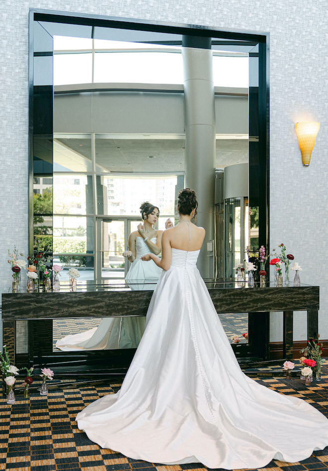 The bride looks at herself in the mirror in the lobby of the Royal Sonesta Houston Galleria as she puts on her perfume. 