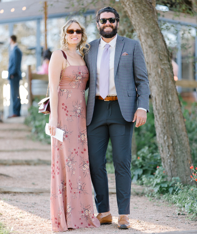 A woman wearing a long pink floral dress standing with a man in a sport coat and tie. 