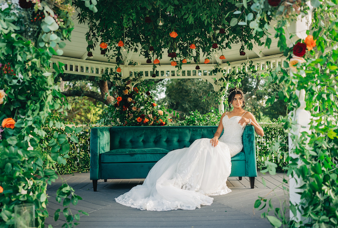 The bride poses on the emerald green couch under the gazebo at her outdoor ceremony at Ashelynn Manor. 