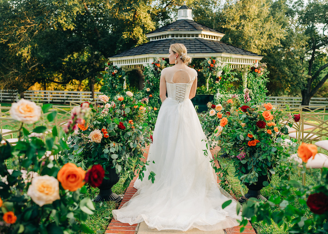 The bride walks down the aisle at her outdoor wedding ceremony to the pavilion detailed in orange, red and pink florals