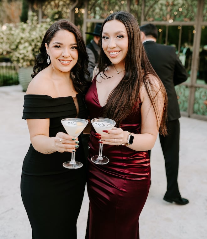 Two women wearing black tie gowns holding cocktails.