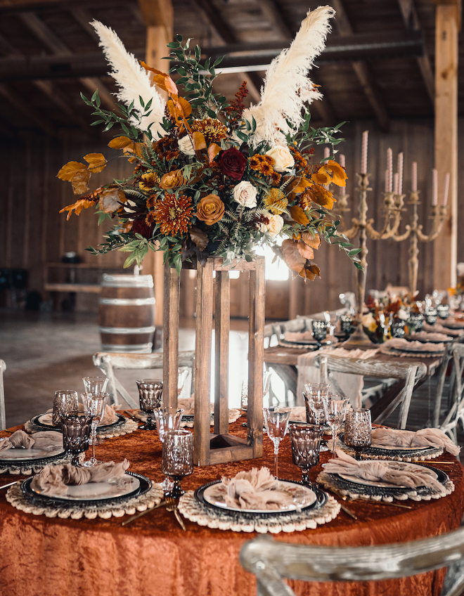 Tall floral centerpieces with pampas grass and burgundy, orange and white flowers decorate the tablespaces. 