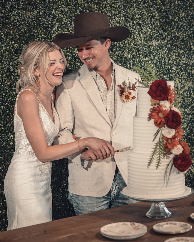 The bride and groom share a laugh as they cute their three-tier white wedding cake. 