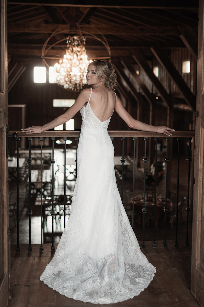 The bride looks over her shoulder as she stands on the balcony overlooking the reception hall. 