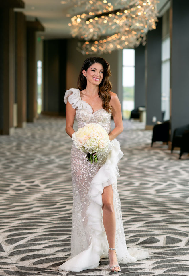 The model smiles while wearing a sparkling wedding gown and holding her bouquet of white and blush colored roses. 