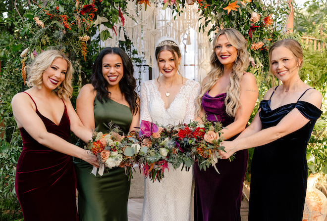 The bride and her bridesmaids pose with their wedding bouquets of dark flowers. 