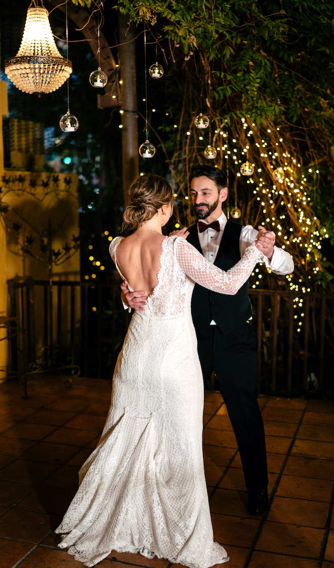 The bride and groom dance under the twinkling lights at their outdoor wedding reception.