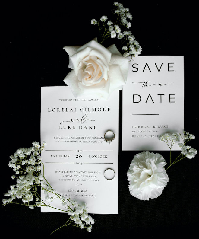 Baby's breath and white roses lay next to black and white wedding stationery. 